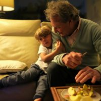 Grandfather and grandson hanging out together in living room couch. Authentic real life family generational relationship at night sitting on couch Grandfather and grandson hanging out together in living room couch. Authentic real life family generational relationship at night sitting on couch