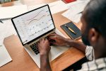 African,Businessman,Analyzing,Statistics,On,Laptop,Screen,,Working,With,Financial African businessman analyzing statistics on laptop screen, working with financial charts on the internet, using business software for data analysis and project management concept, close-up rear view