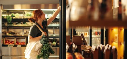 Female,Customer,Choosing,Food,Products,From,A,Shelf,While,Carrying Woman shopping for CPG goods on the grocery shelf